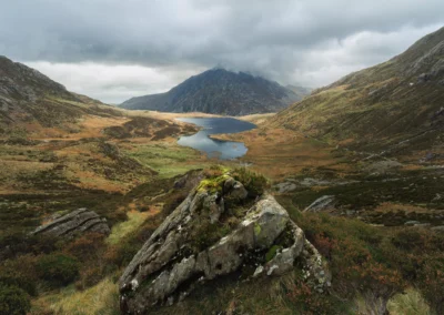 An elevated view looking down into Cwm Idwal, Snowdonia, with Llyn Idwal visible far below, the valley floor in rich autumn colour and Pen yr Ole Wen rising beyond