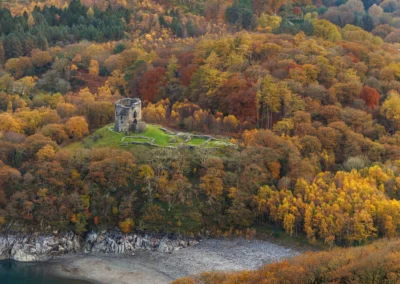 An aerial bird's-eye view of Dolbadarn Castle tower surrounded by a dense canopy of orange and yellow autumn trees.