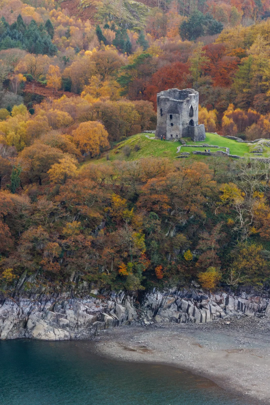An elevated view of the round stone tower of Dolbadarn Castle overlooking Llyn Peris and the Llanberis Pass.
