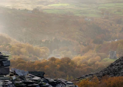 A distant view of Dolbadarn Castle tower sitting on a rocky outcrop surrounded by misty autumn woods and Llyn Peris.