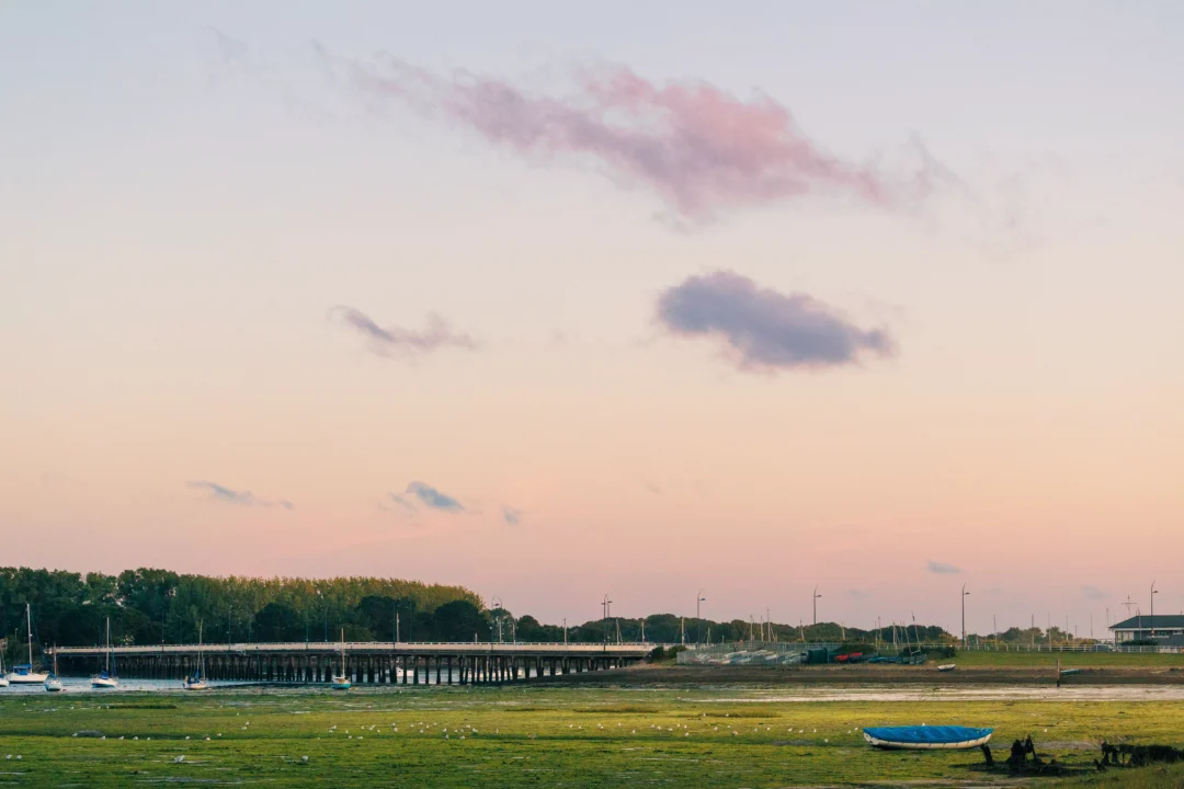 Soft pink and blue dawn sky above the wooden bridge structure with a solitary blue boat on green marshland.