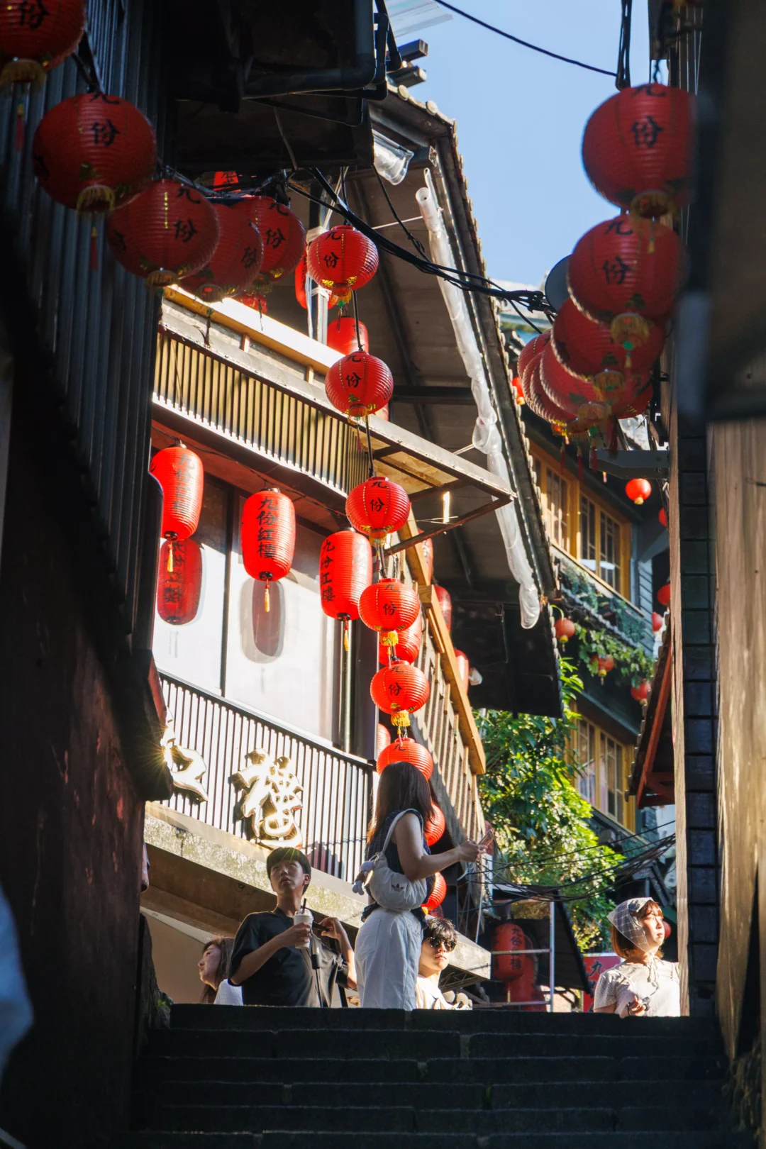 Amei Teahouse staircase in Jiufen with red lanterns, ivy walls and small bronze statues at the base