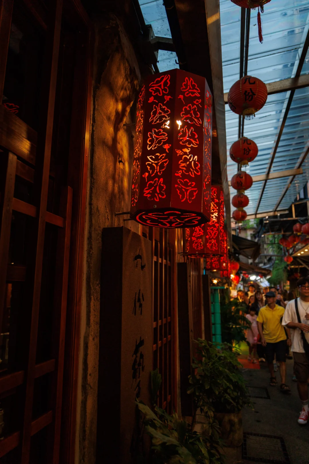 Close-up of an ornate cut-out red lantern glowing at dusk in Jiufen with a blue sky background