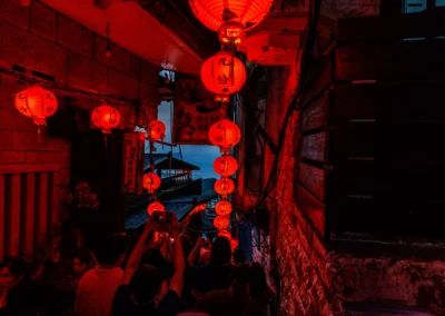 Narrow Jiufen alleyway bathed in deep red lantern light at night with crowds and the dark sea visible at the end