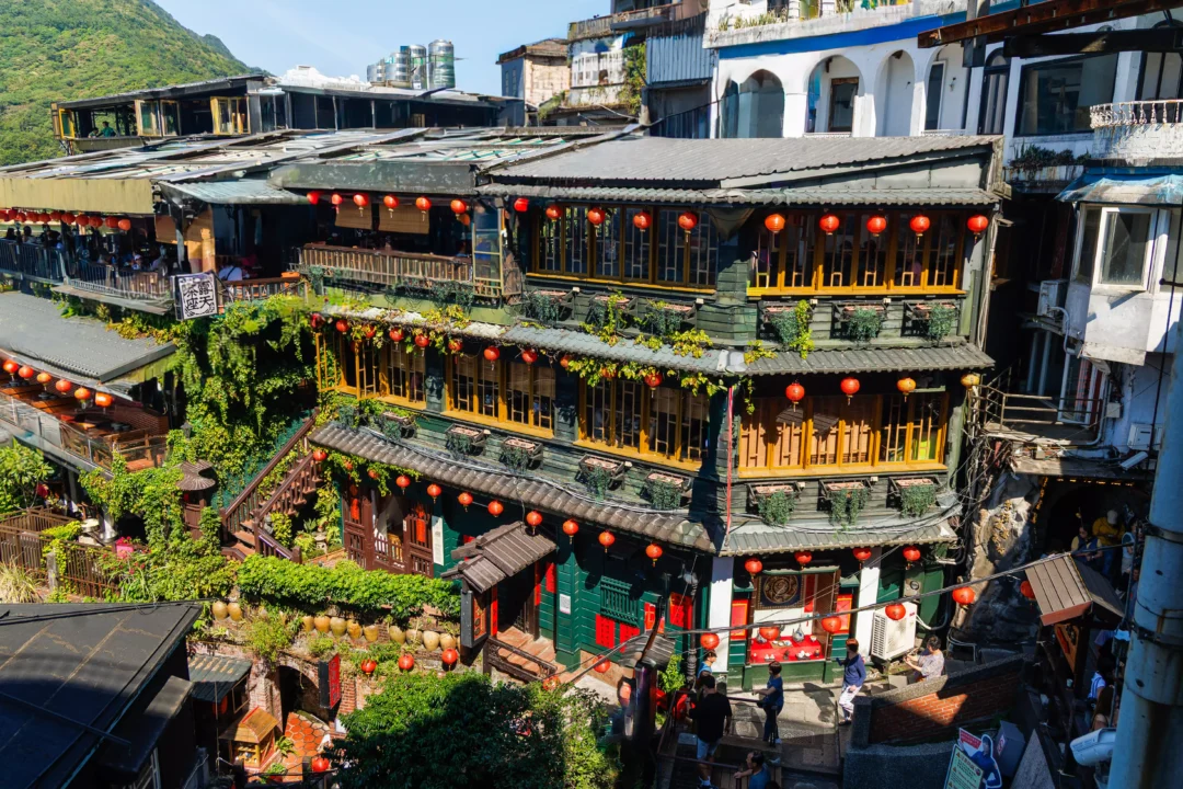 Iconic Jiufen teahouse building covered in red lanterns and cascading ivy seen from the hillside steps