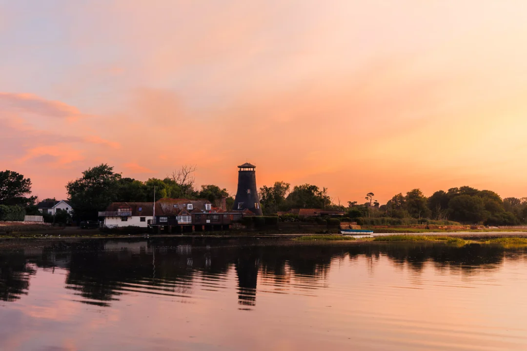 The iconic windmill and waterfront buildings casting clear reflections into smooth water under an orange sky.