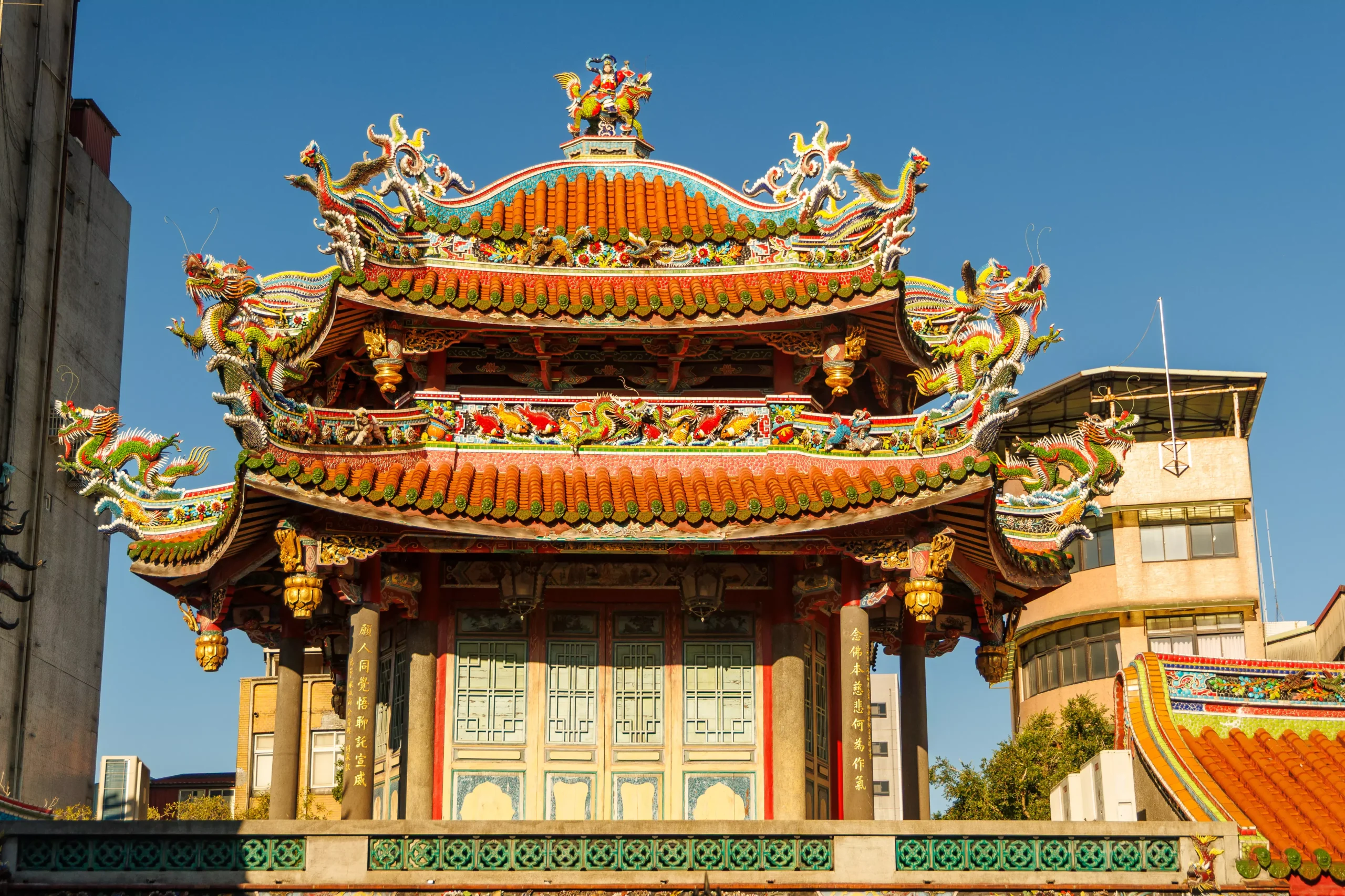 longshan-temple-taipei-facade-blue-sky Ornate facade of Longshan Temple Taipei with colourful dragons and tiled rooftop against blue sky