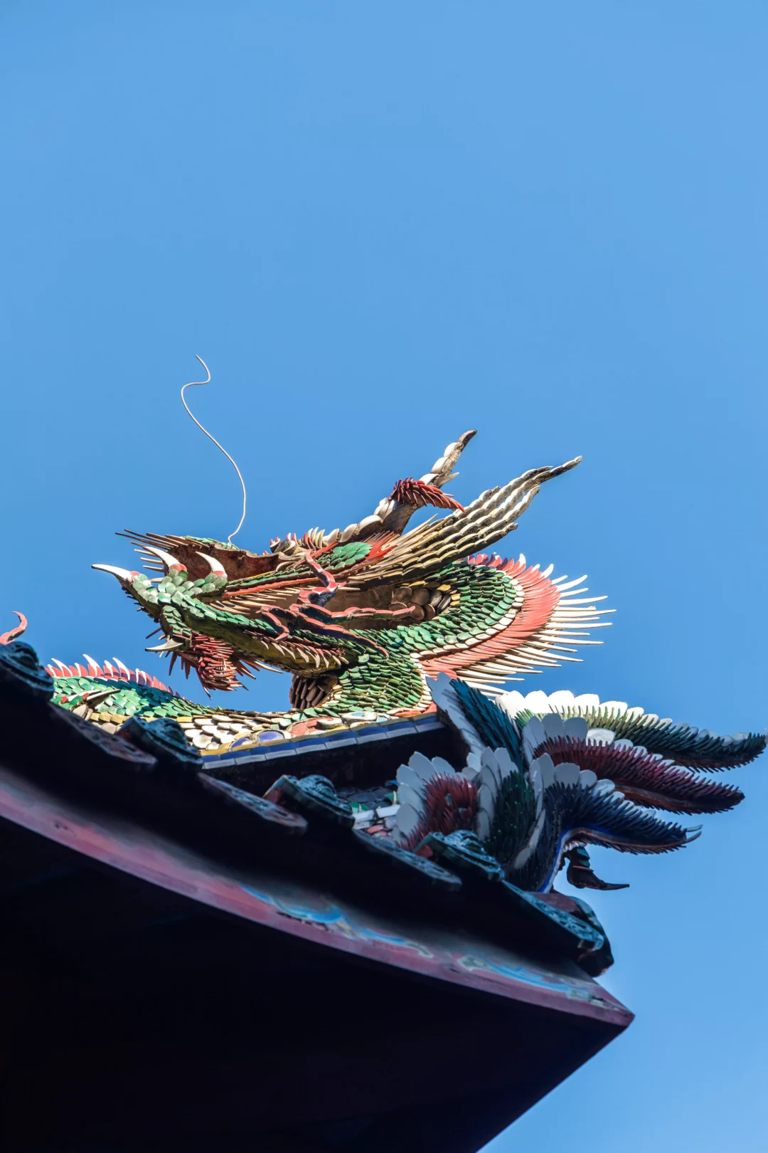 Close-up of a jewel-coloured phoenix roof ornament on Longshan Temple against deep blue sky