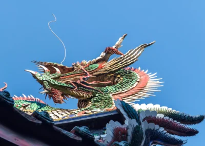 Close-up of a jewel-coloured phoenix roof ornament on Longshan Temple against deep blue sky