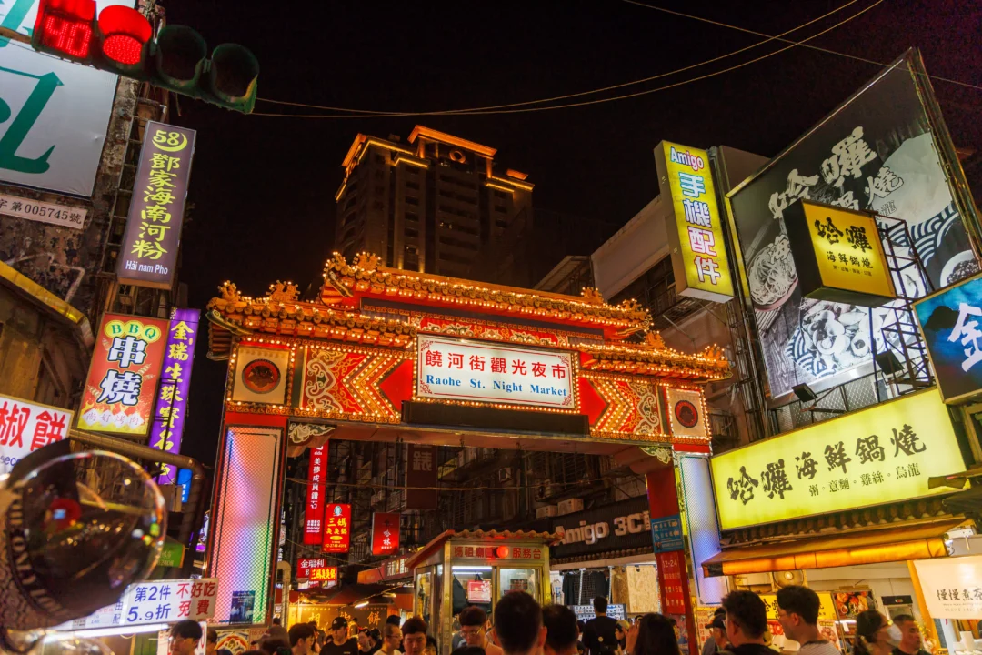 Raohe Street Night Market illuminated entrance gate glowing with neon signs and lanterns at night