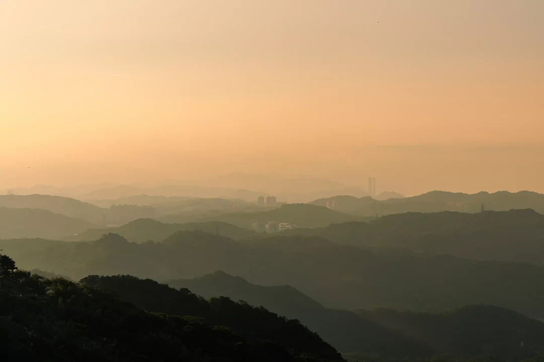 Layered mountain silhouettes receding into golden orange haze at sunset above Taiwan's northeast hills
