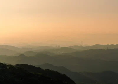 Layered mountain silhouettes receding into golden orange haze at sunset above Taiwan's northeast hills