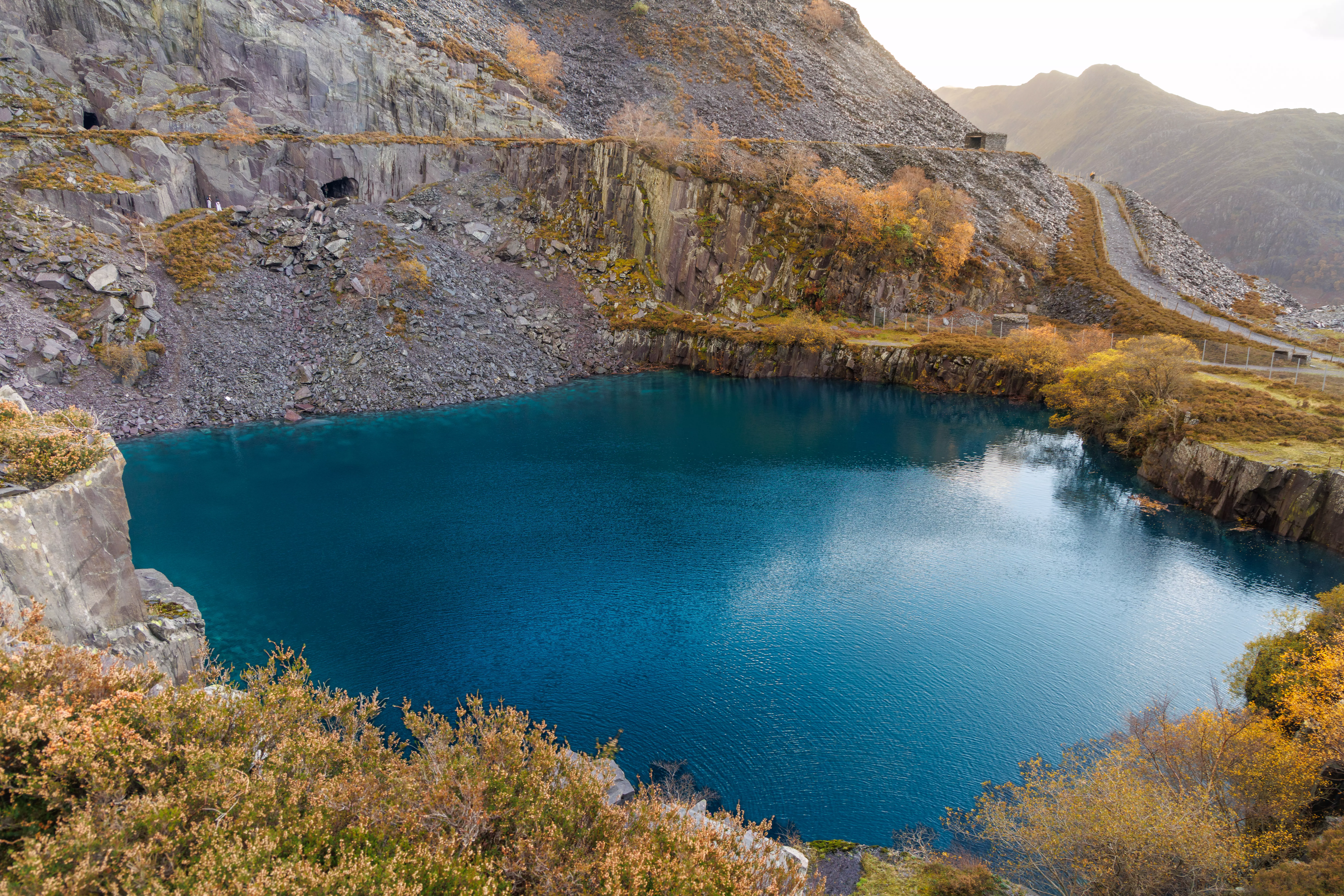 A deep, flooded quarry pit with striking turquoise water and high slate gallery walls.