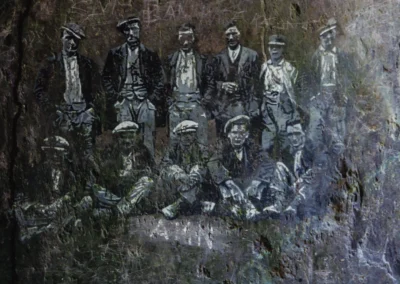 A detailed white-line engraving on a dark slate slab depicting a bearded quarry worker with a mustache and hat.
