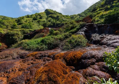Wide view of Xiaoyoukeng volcanic area with red mineral rock formations and a small waterfall among green vegetation