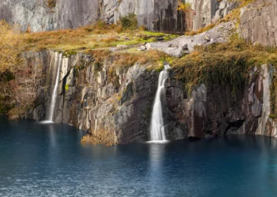 A moody, low-light landscape showing the dark silhouettes of mountains flanking Llyn Peris with soft light on the water.