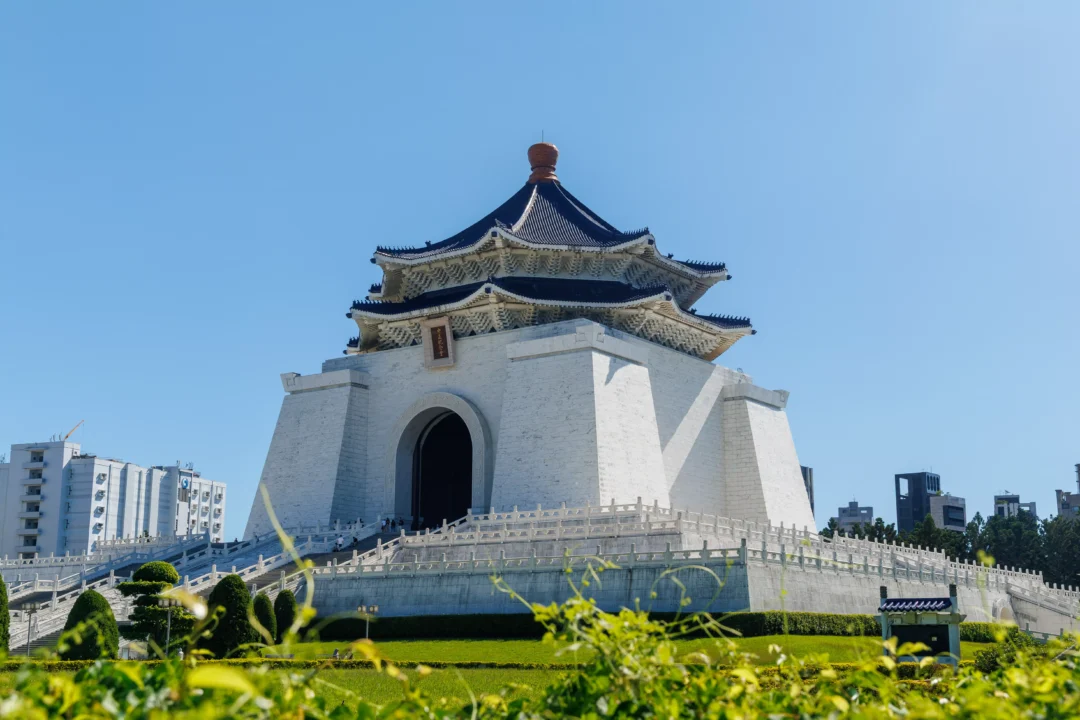 Chiang Kai-shek Memorial Hall rising above manicured hedges and gardens, viewed from low angle with blue sky
