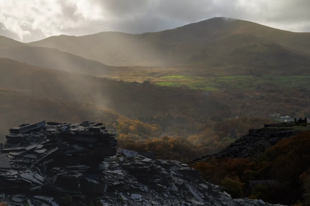 Dramatic sunbeams shining through clouds over the Llanberis Pass with sharp slate rocks in the foreground