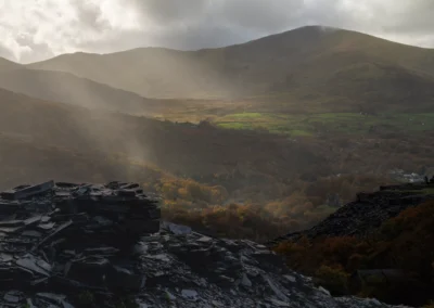 Dramatic sunbeams shining through clouds over the Llanberis Pass with sharp slate rocks in the foreground