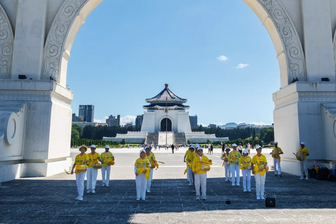 Group of performers in yellow uniforms playing drums framed through a white arch of the Liberty Square gate, with Chiang Kai-shek Memorial Hall visible in the distance