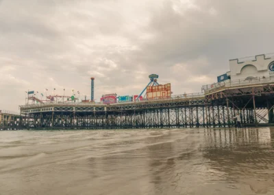 Wide-angle view of the historic pleasure pier and its colourful fairground rides under a dramatic, overcast sky.
