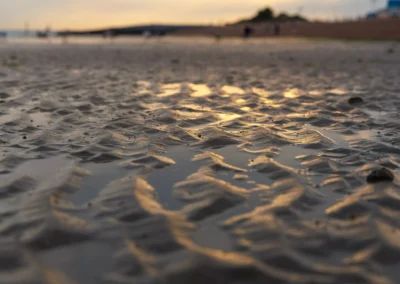 Low-angle shot of textured sand ridges holding small pools of water that catch the golden evening light.