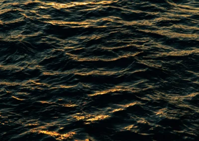 Close-up texture of dark, rhythmic ocean waves catching the glinting metallic highlights of a coastal sunset.