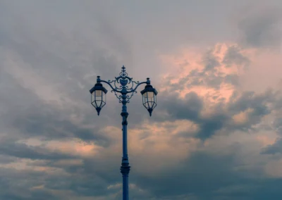 A dark silhouetted Victorian-style lamp post stands against a turbulent canvas of bruised purple and coral sunset clouds.