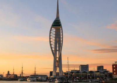 The iconic white Spinnaker Tower rising above Portsmouth Harbour during a glowing golden hour sunset with calm waters below.