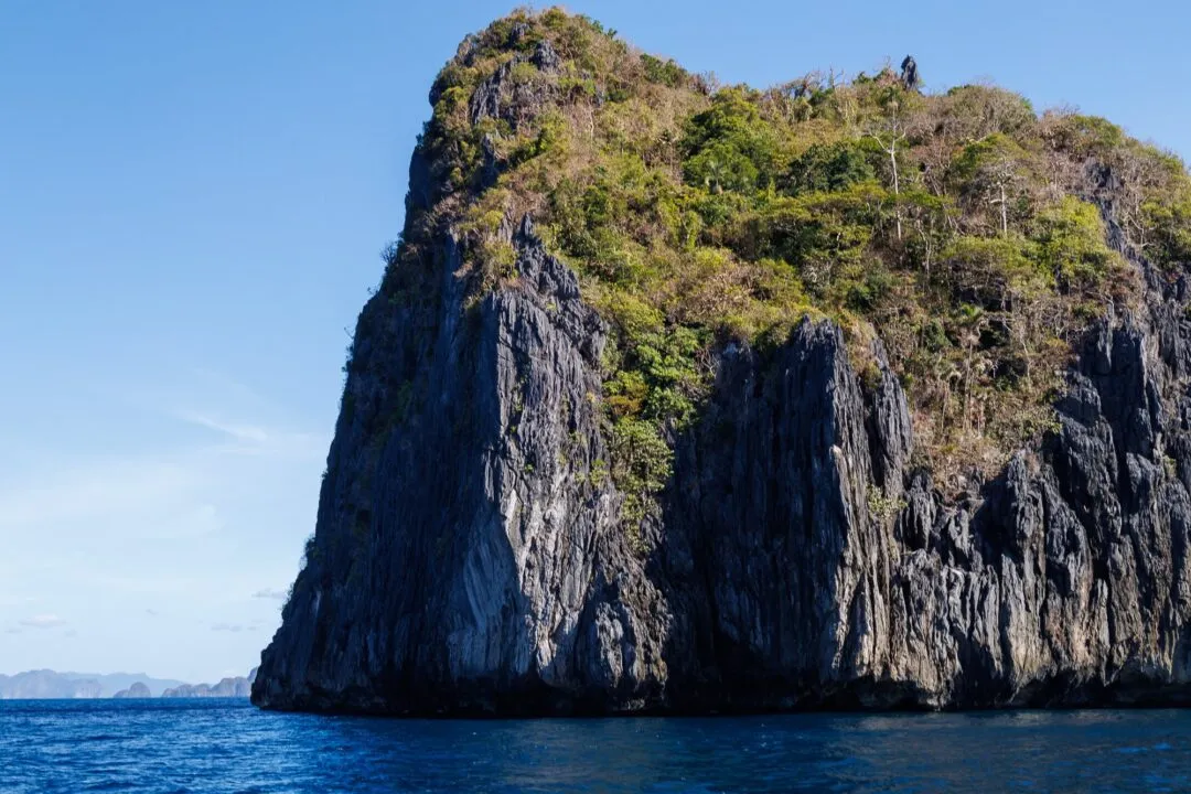 Backlit jungle topped karst cliff blue water El Nido
