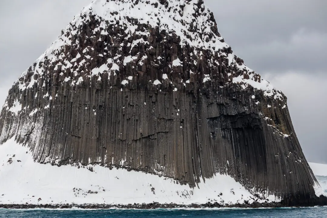 Dense black basalt columns of a sea stack dusted with snow, Antarctica