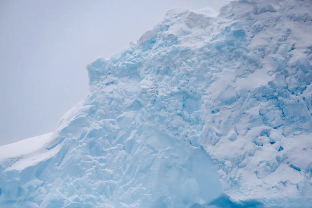 Glowing blue ice archway reflected in still water with icebergs beyond, Antarctica