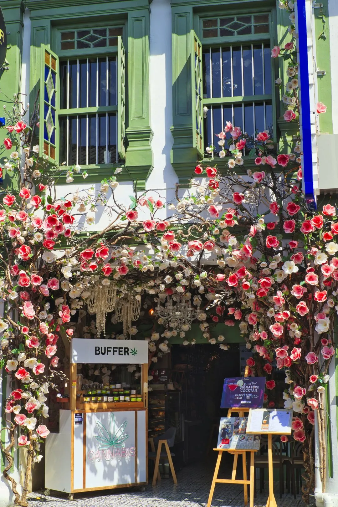 A shophouse storefront draped in pink and white flowers in Phuket Old Town.