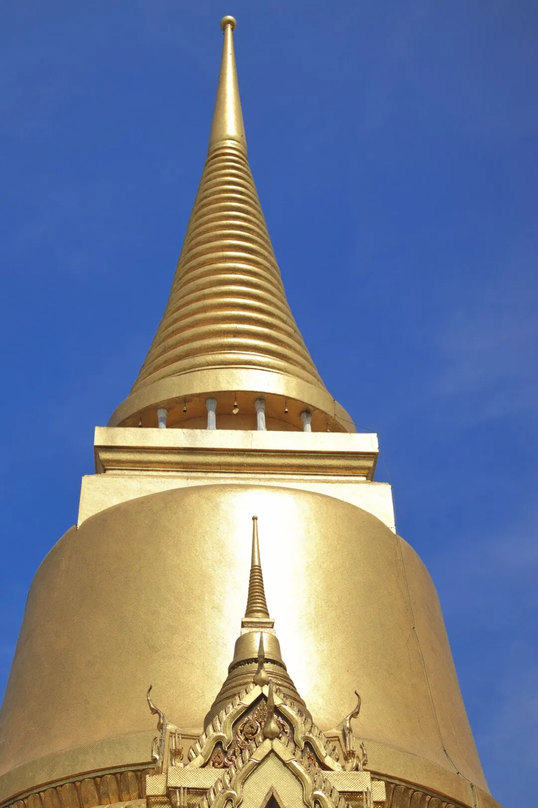 A gilded chedi spire isolated against a clear blue sky at a Bangkok temple complex.