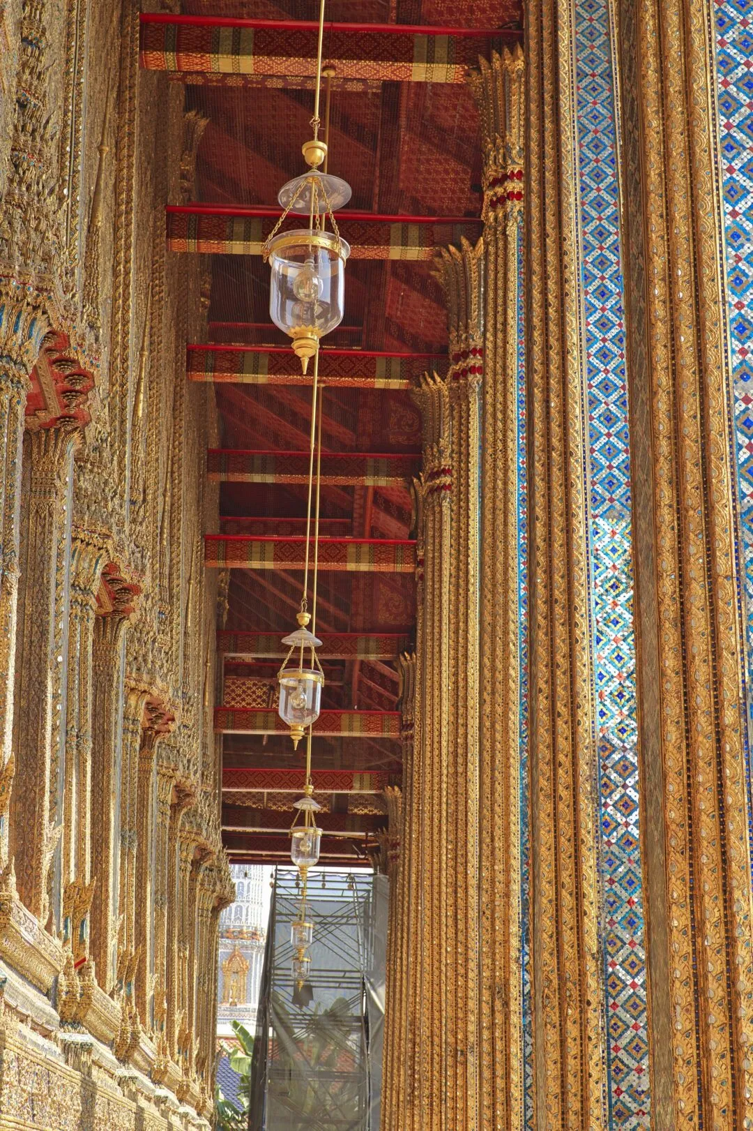 Hanging glass lanterns receding down a gilded temple colonnade in Bangkok, Thailand.