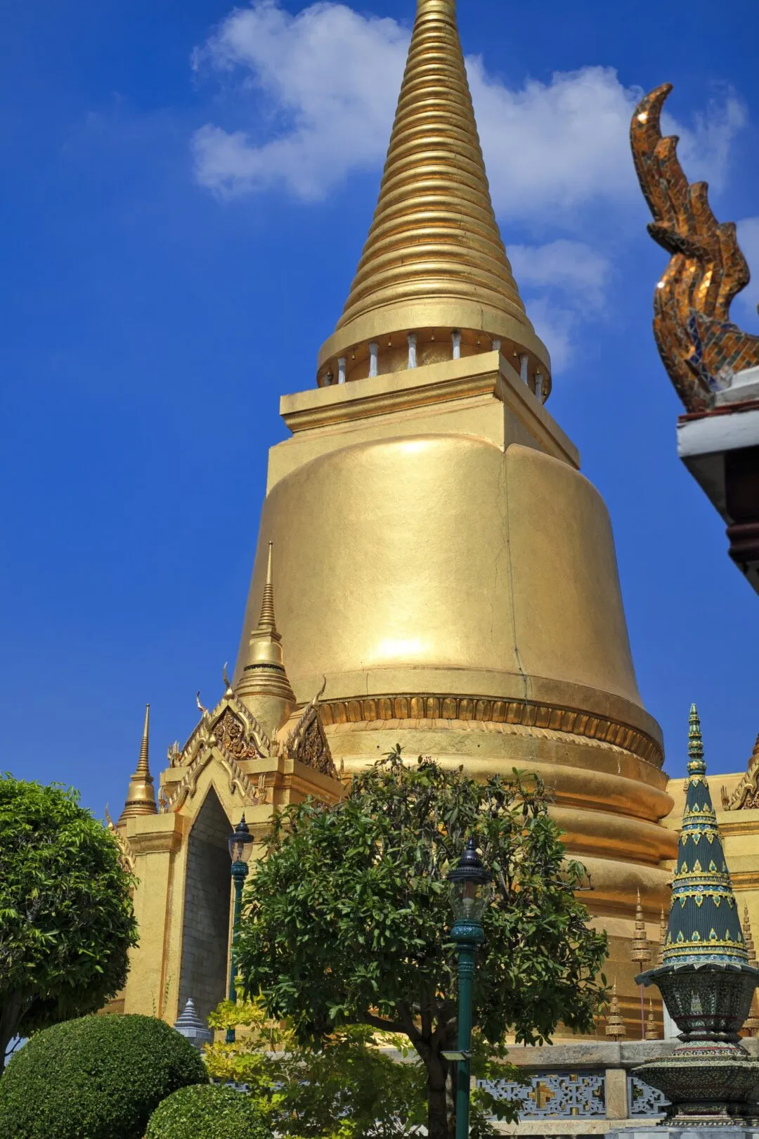 A gold-leafed stupa framed by soft foliage against a clear sky in Bangkok.