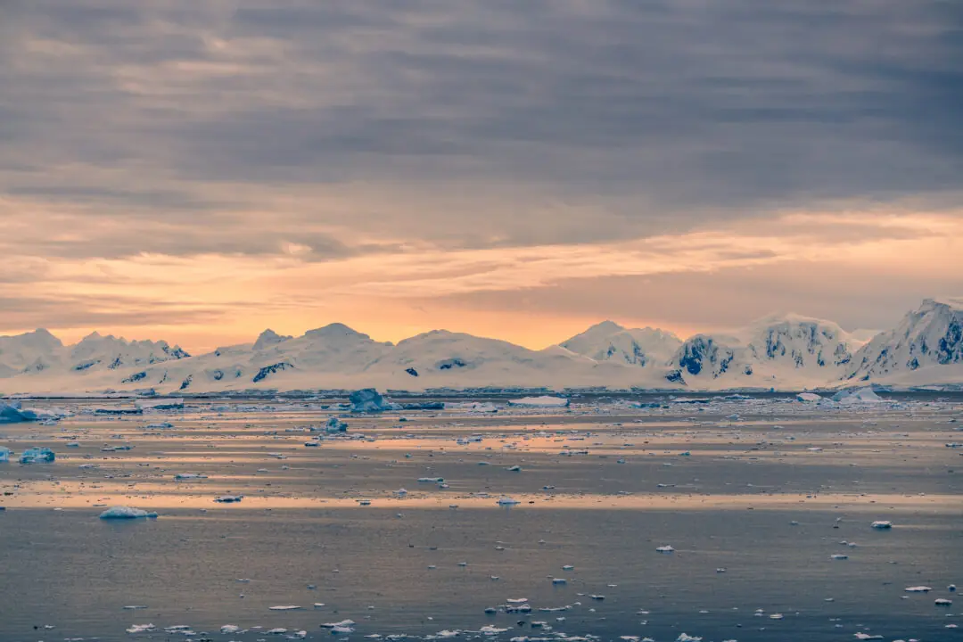 Wide golden-hour panorama of sea-ice-strewn water before soft mountain silhouettes, Antarctica