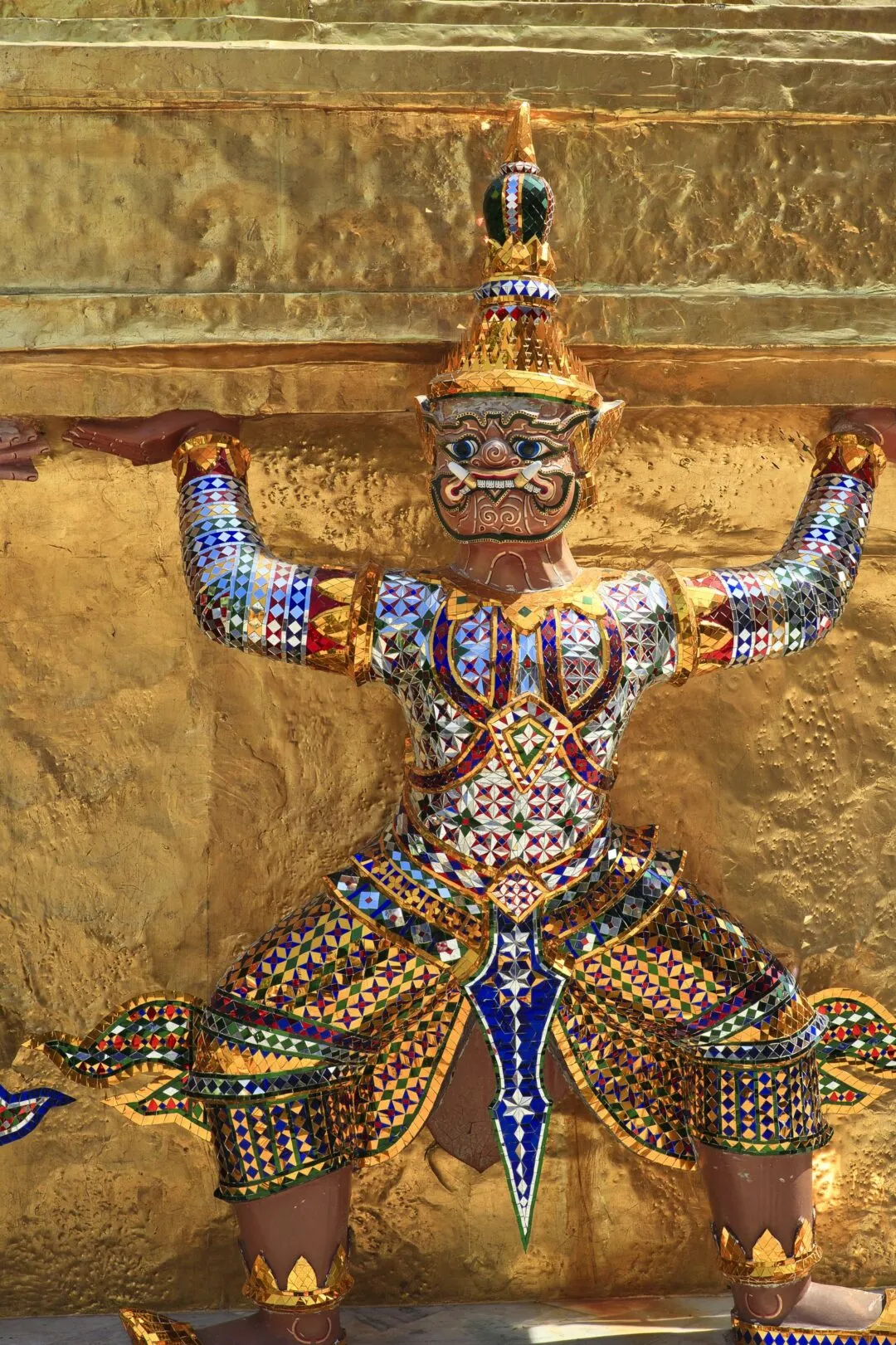 A mosaic-armoured guardian yaksha statue against a glowing gold temple wall in Bangkok.