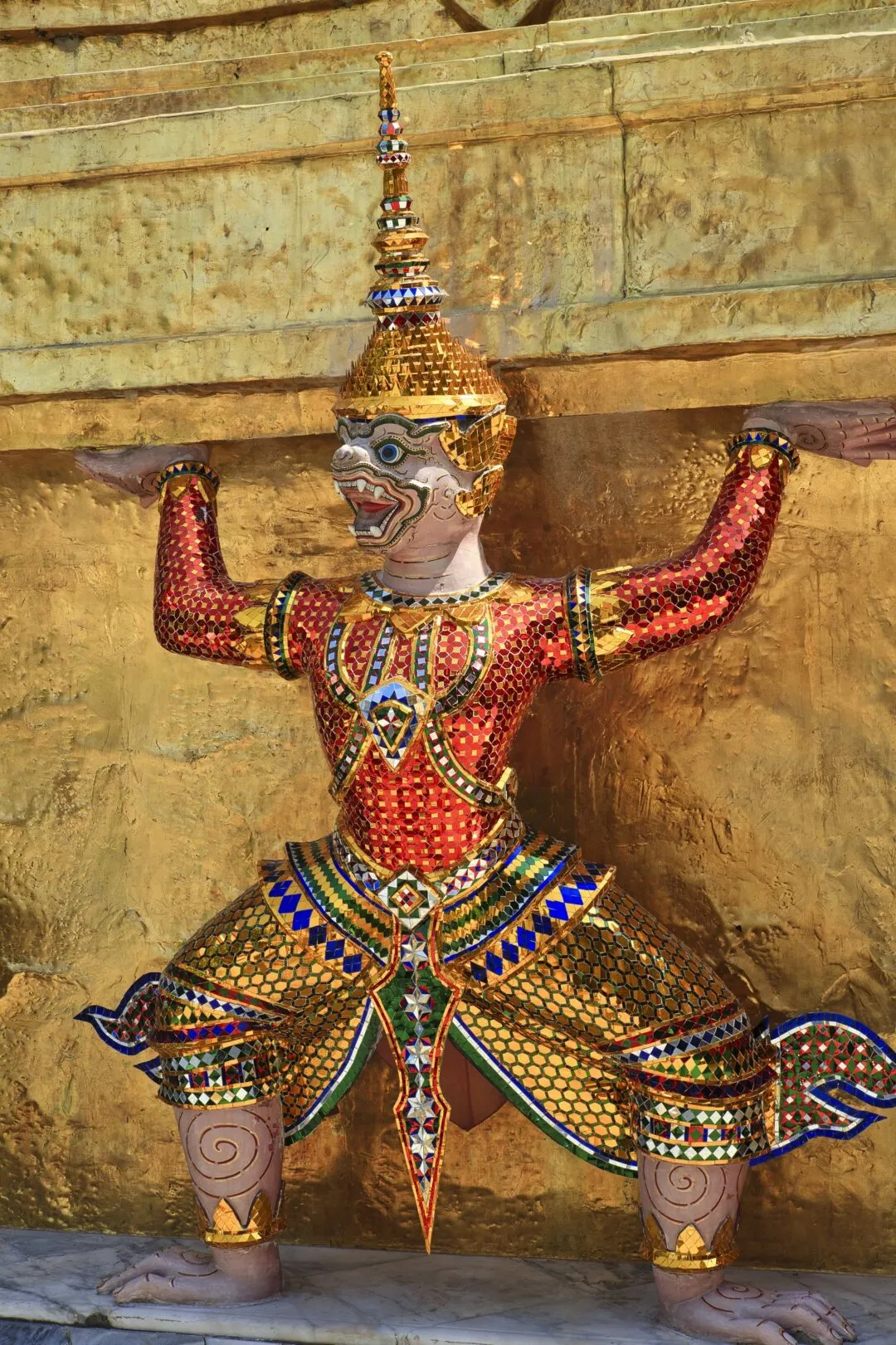 A guardian yaksha statue in red and gold at a Bangkok temple complex.