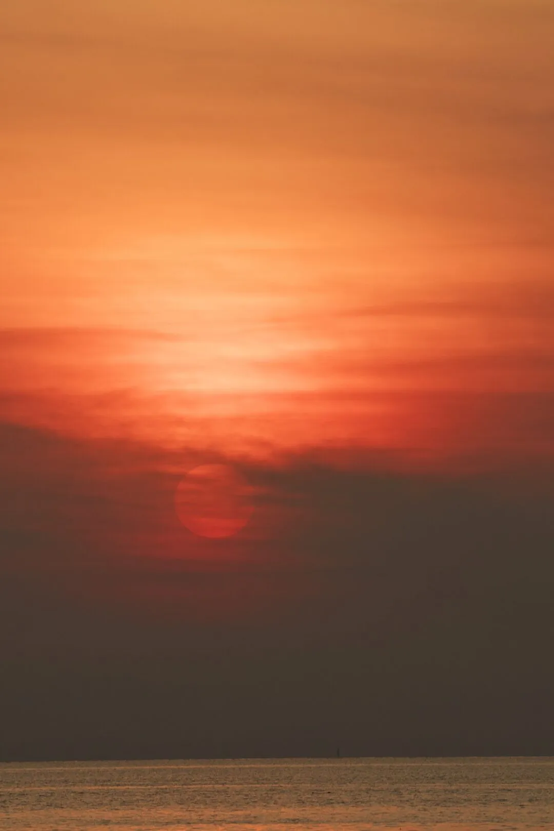 A hazy sun setting low over open sea in a minimalist seascape composition, Thailand.
