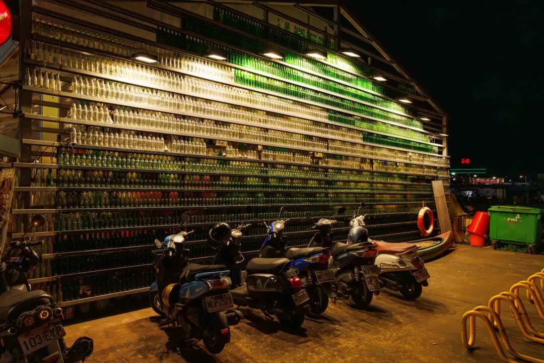 Graphic wall of stacked soda bottles lit warm gold with a passing scooter, Hualien, Taiwan