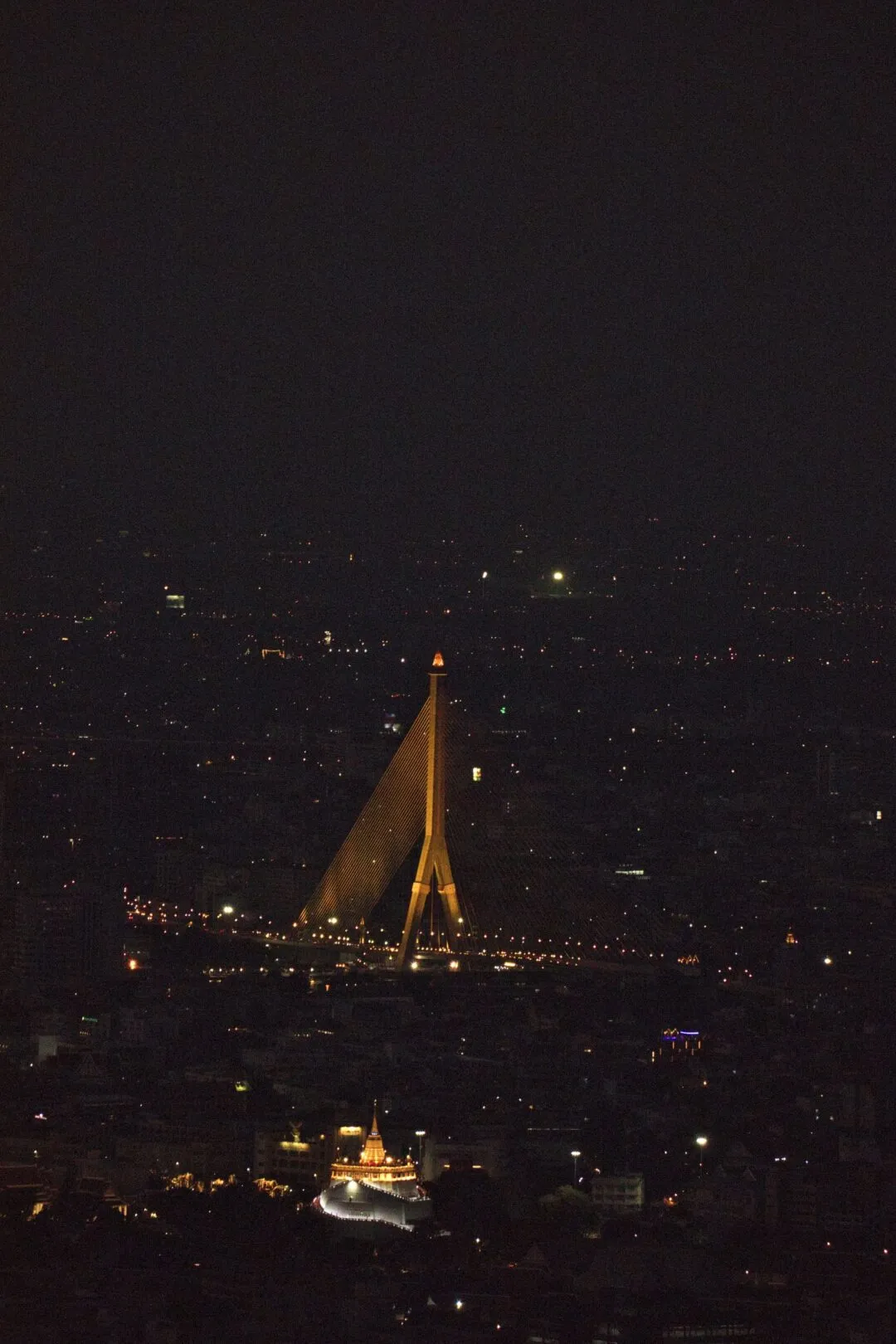 An illuminated cable-stayed bridge silhouette with a glowing temple in the foreground, Bangkok.