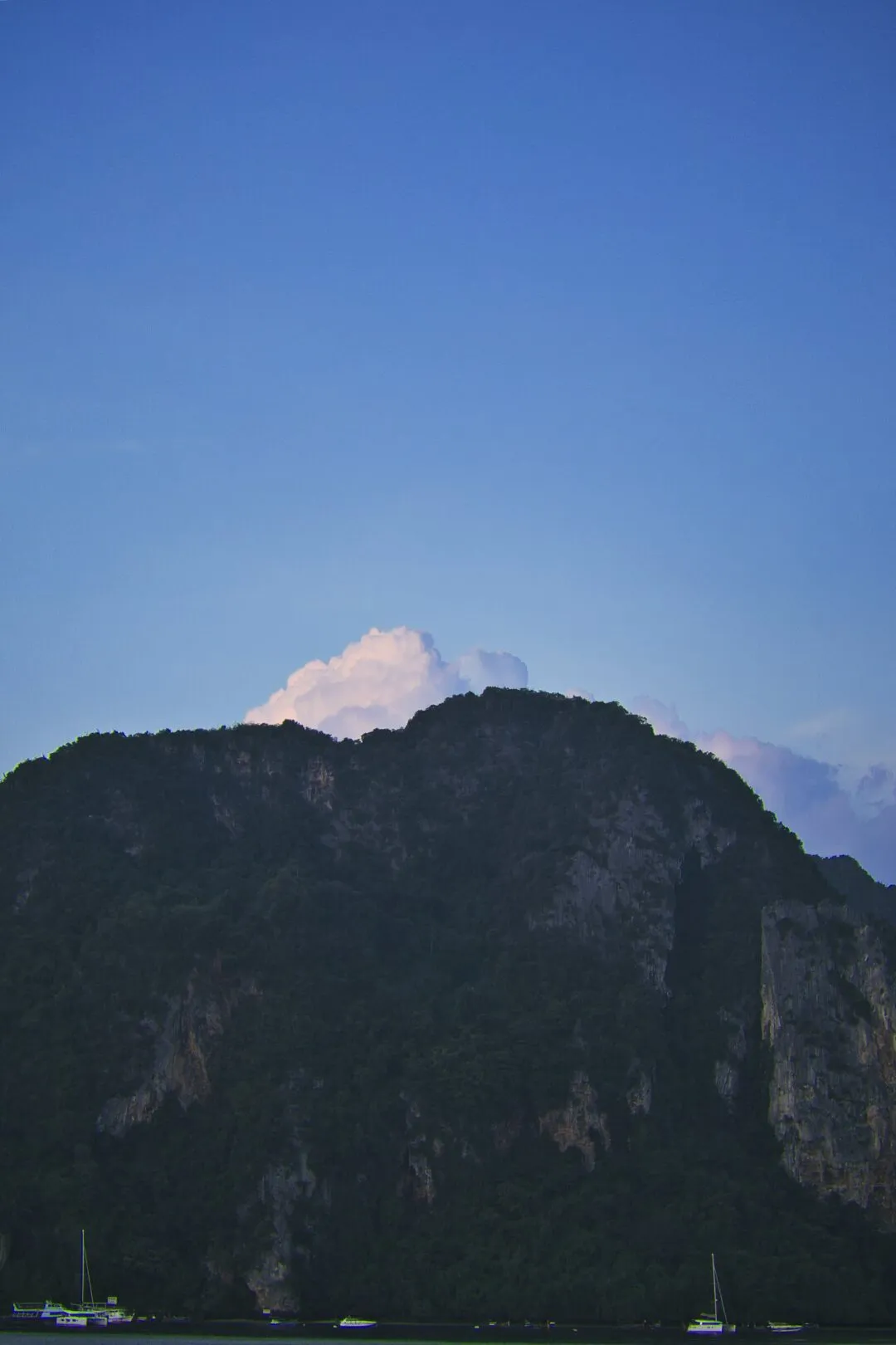 A karst island silhouette at twilight with small boats on the water in Thailand.