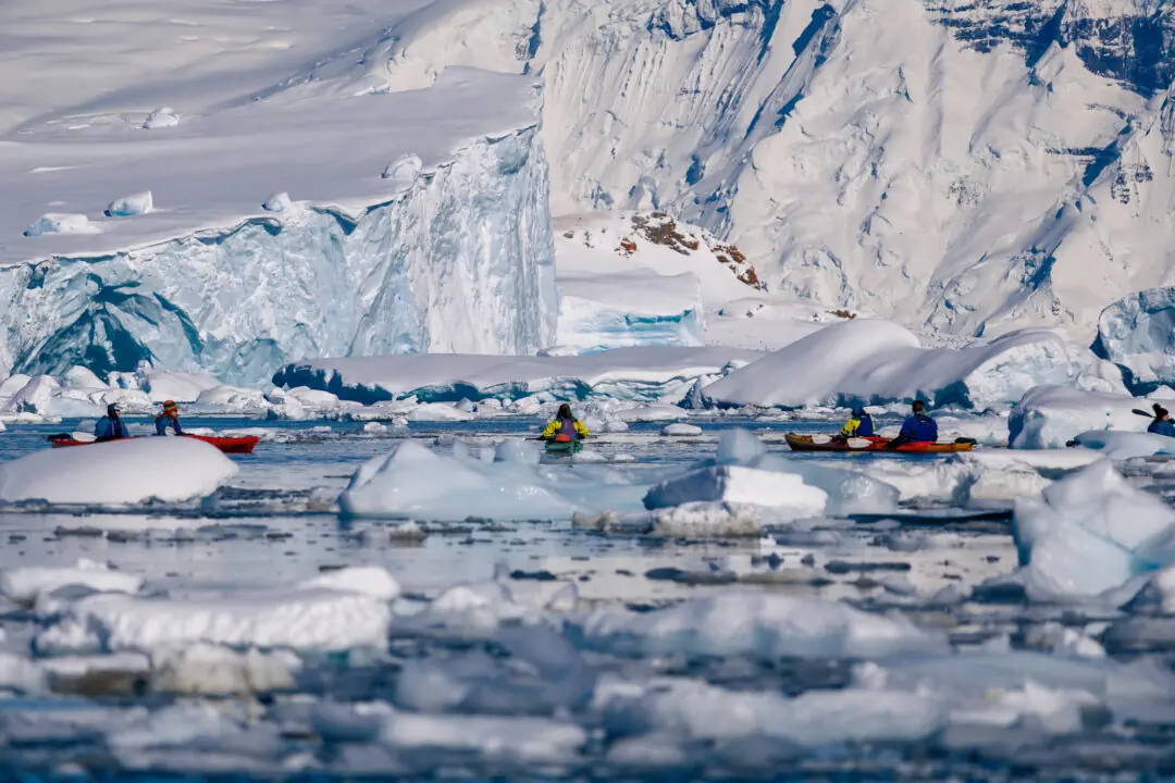 Kayakers dwarfed beneath a massive ice cliff among scattered icebergs, Antarctica