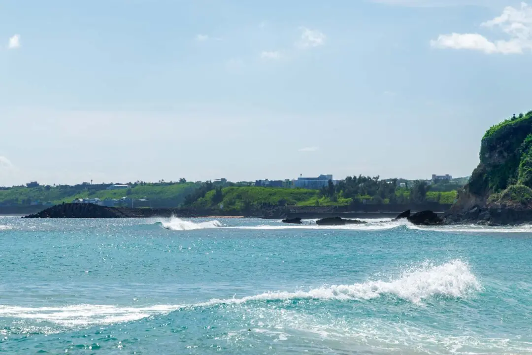 Clean coastal bay with cliff and distant town under calm waves, Kenting, Taiwan