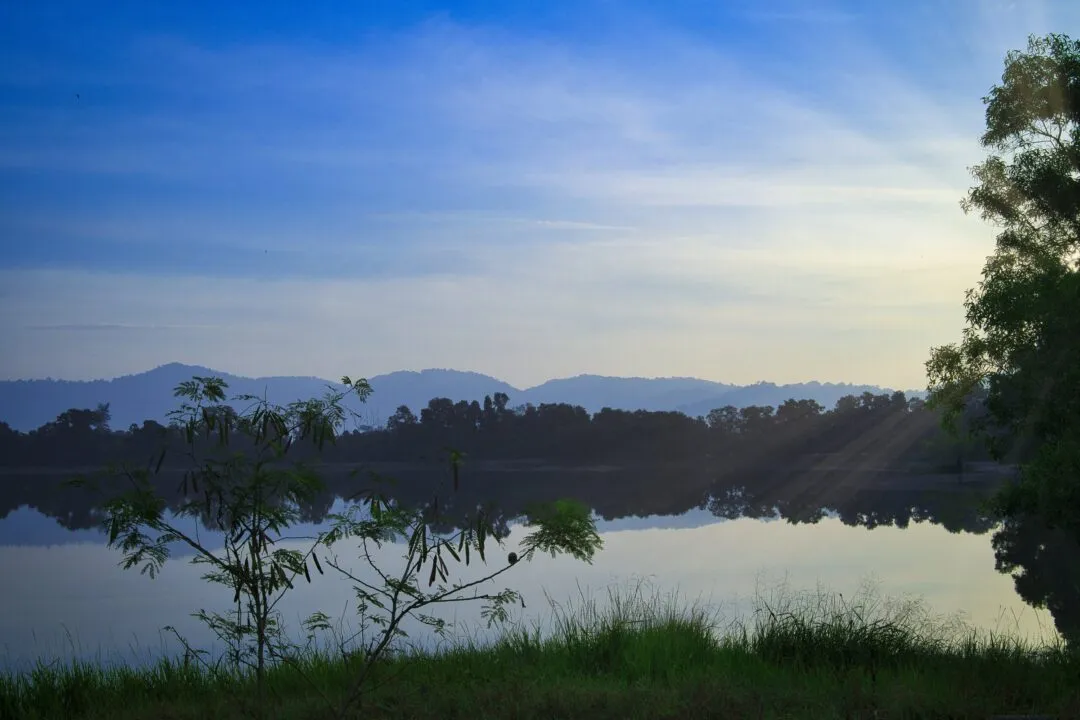Layered mountain silhouettes reflected in a calm lake at sunrise in Thailand.