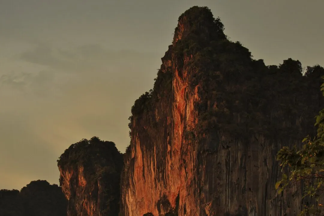 A close telephoto view of limestone karst cliff faces glowing orange at golden hour in Thailand.