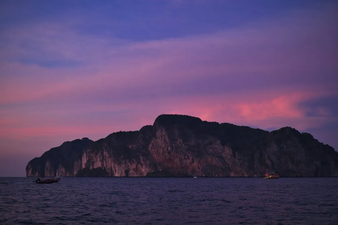 A dramatic limestone island silhouette under a pink and violet sunset sky in Thailand.