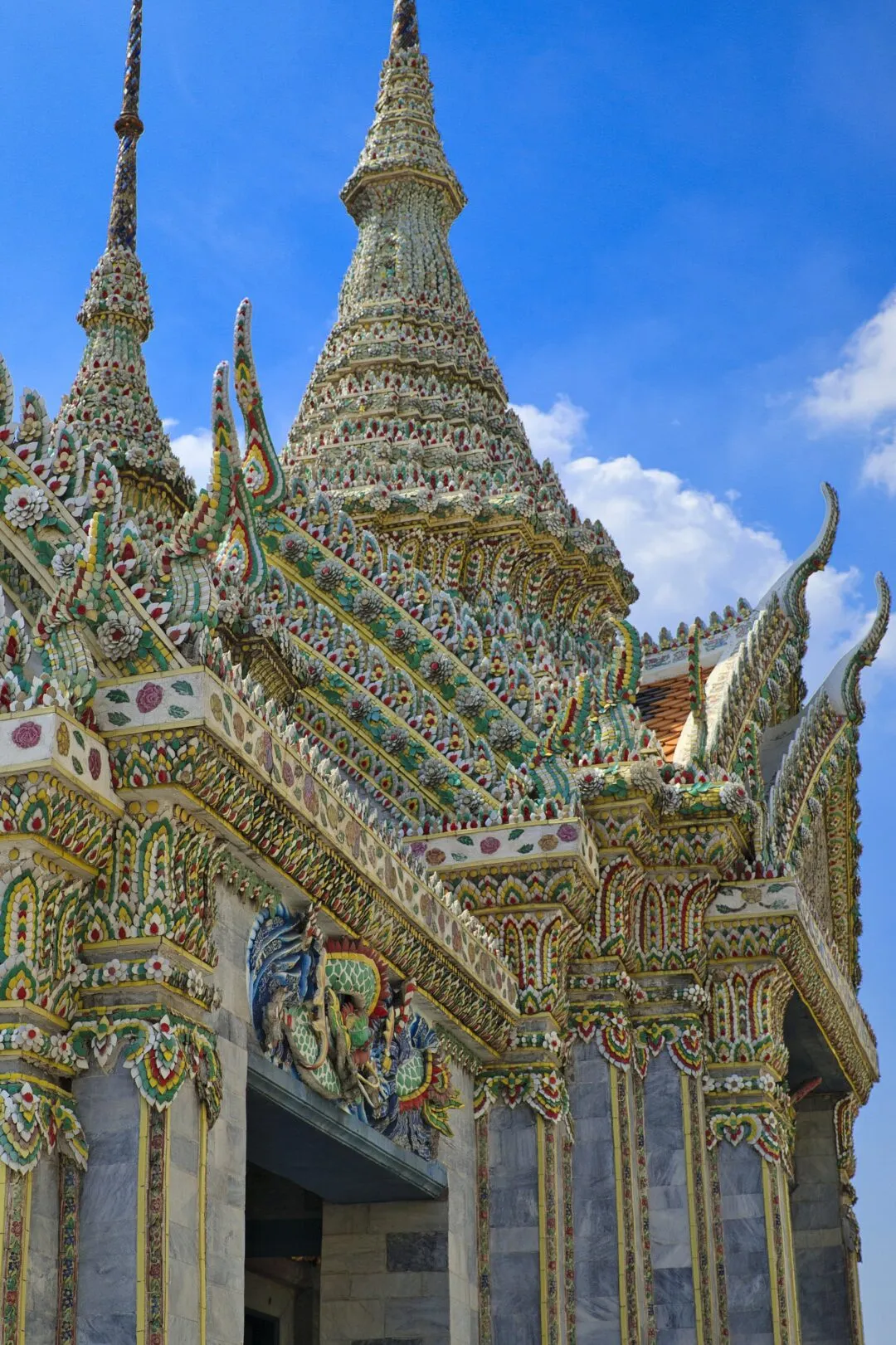 A green and white mosaic-tiled temple spire on a diagonal against deep blue sky in Bangkok.