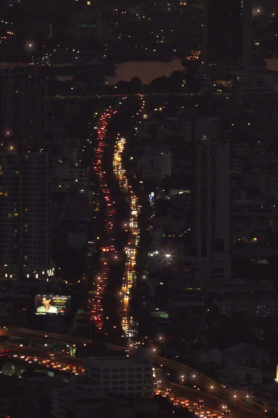 Red and white traffic light trails winding through a busy Bangkok road at night.